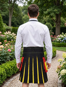 A man viewed from behind wearing a white long-sleeve shirt and a black pleated kilt with bold yellow vertical stripes and red side panels, standing on a gravel garden path surrounded by greenery and flowers.